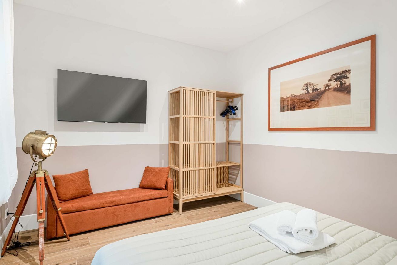 Una camera da letto con un letto, un armadietto in legno, un divano, una TV e un quadro appeso al muro.