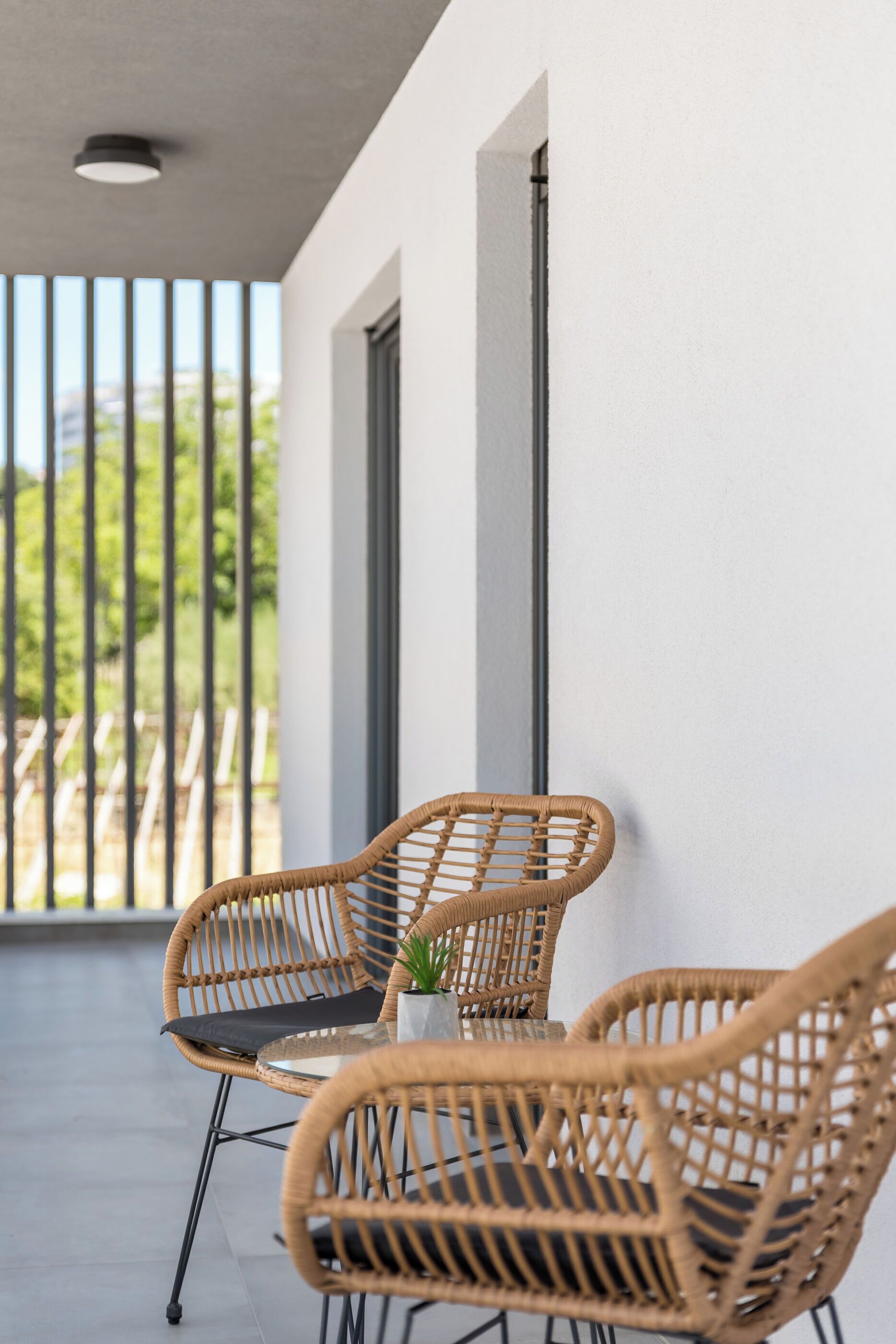 A balcony with wicker chairs and a table, overlooking a garden.