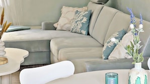 Ein modernes Wohnzimmer mit einem grauen Ecksofa, einem runden weißen Tisch und einer dekorativen Vase mit blauen Blumen.