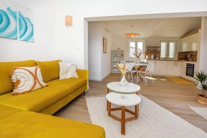 A modern living room with a yellow sofa, white rug, and a dining area with a white table and chairs. - Apartments Laganini (Primosten)