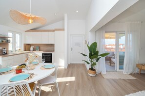 A modern kitchen with white cabinets, a dining area with a round table, and a large potted plant. - Apartments Laganini (Primosten)