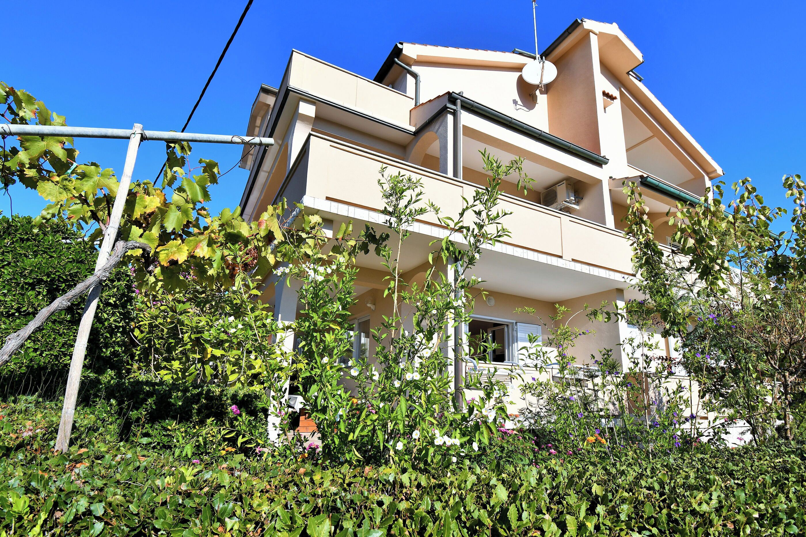 A two-story building with a balcony, surrounded by greenery and a fence.