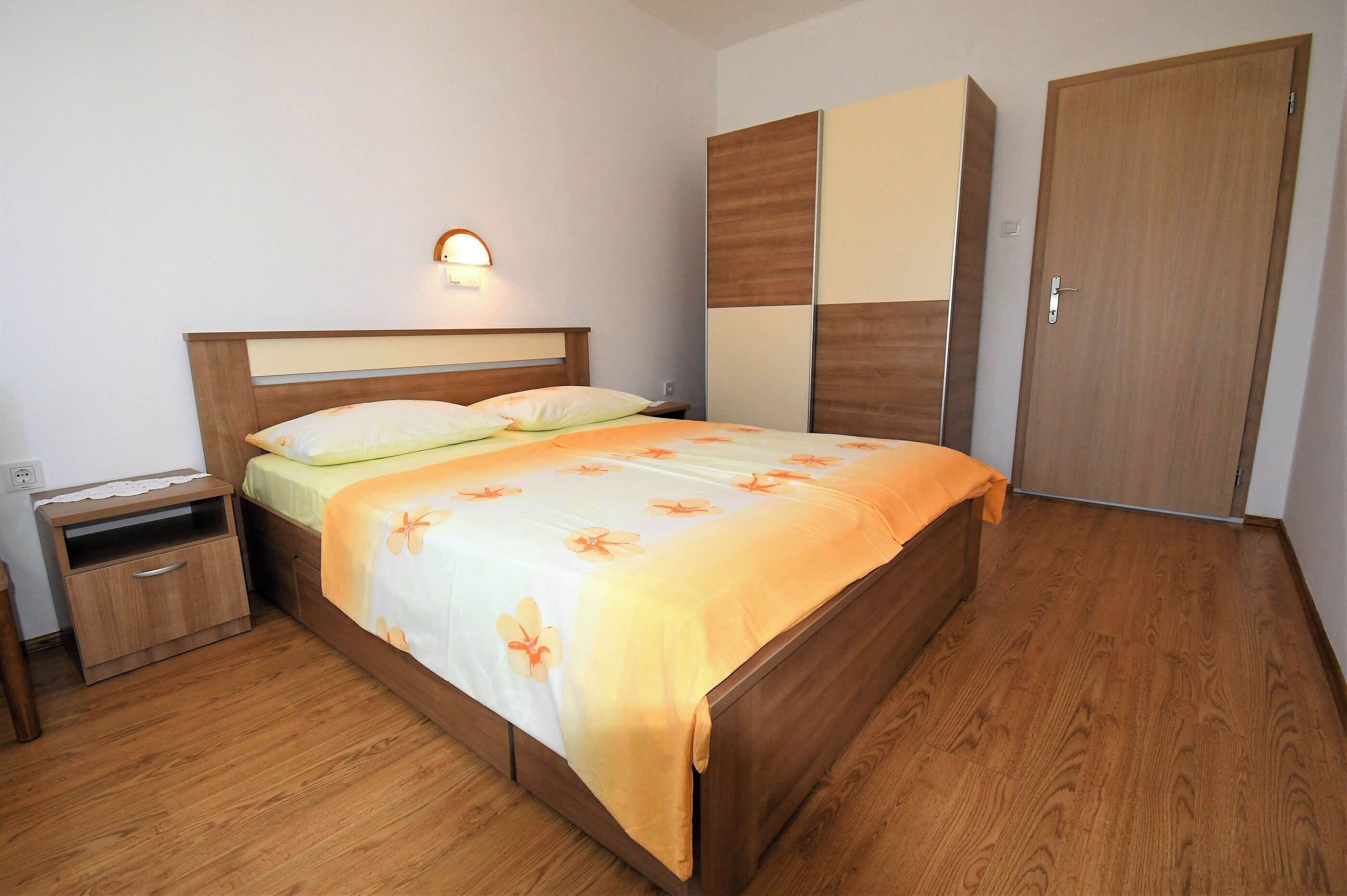 Une chambre à coucher avec un lit en bois, une table de chevet, une armoire et une lampe fixée au mur.