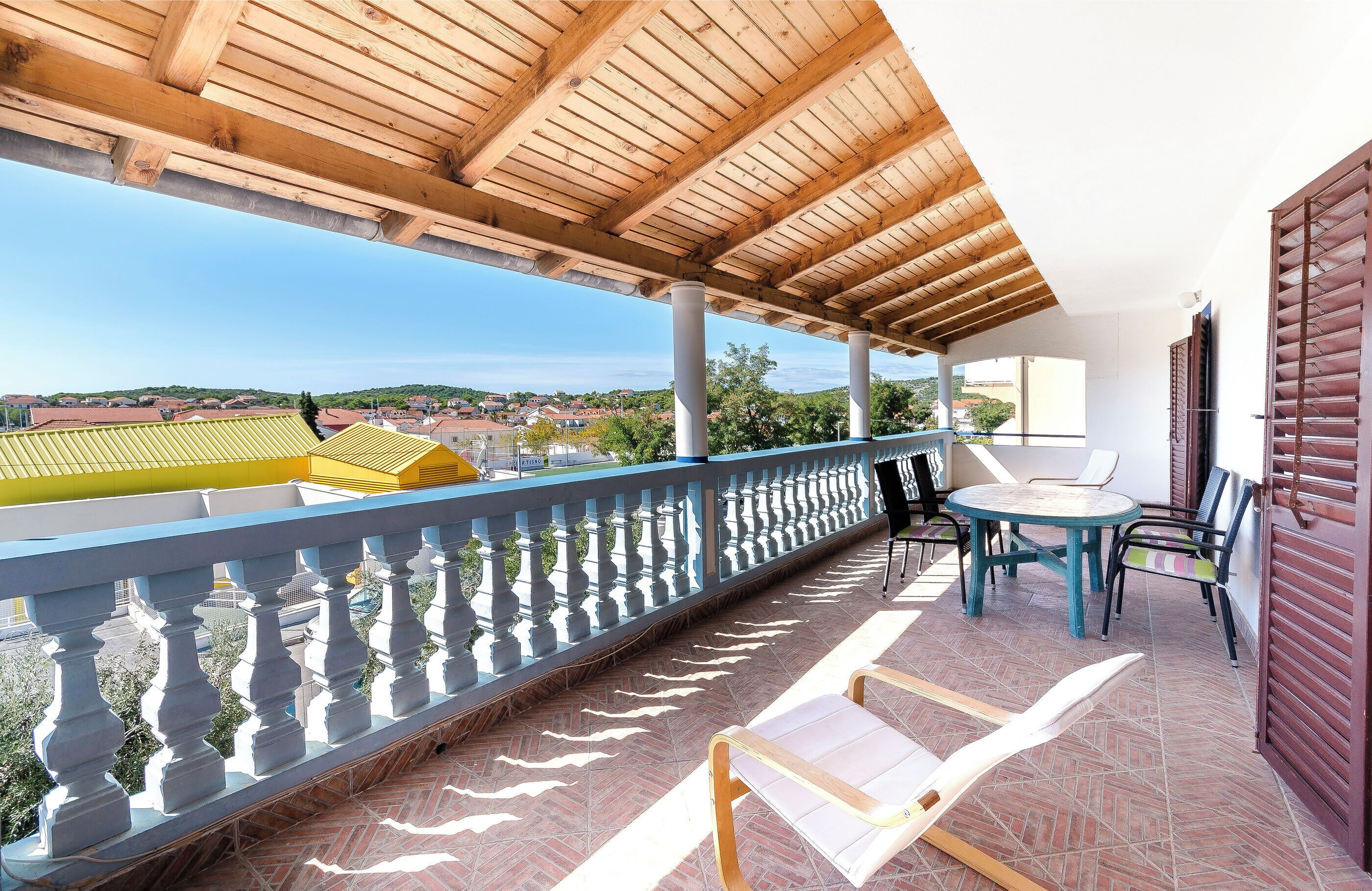 A balcony with a wooden ceiling, a view of the city, and a table with chairs.