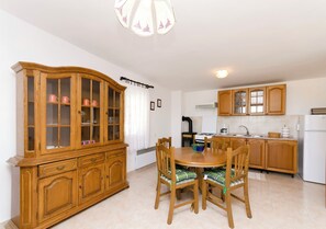 A dining area with a wooden cabinet, a round table, and chairs. - Apartments Jerko (Tisno)