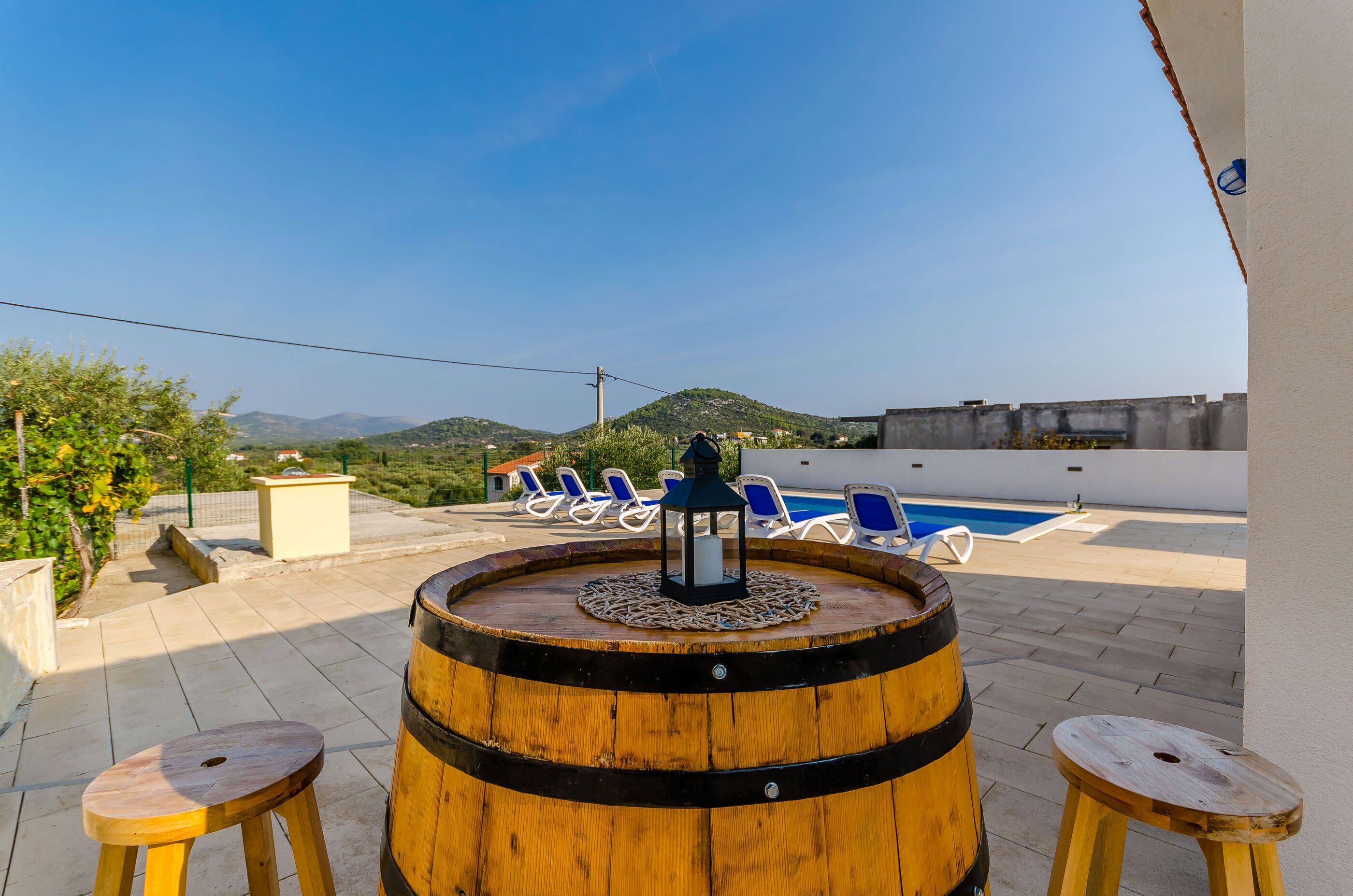 A rooftop terrace with a wooden barrel, two stools, and a poolside area with blue chairs.
