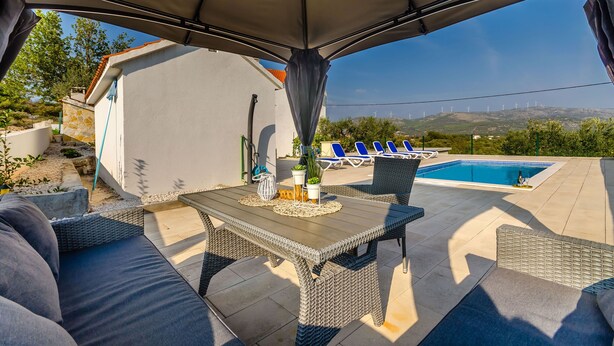 An outdoor patio with a table and chairs, a pool, and lounge chairs. - House Roko (Marina)