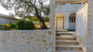 A stone staircase leading to a white door with a yellow diamond pattern, surrounded by a stone wall and greenery. - House Roko (Marina)