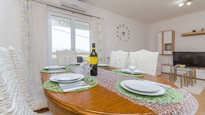 A dining area with a wooden table set for four, a bottle of wine, and a clock on the wall. - House Roko (Marina)