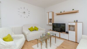 A modern living room with a white sofa, a glass coffee table, a TV, and a wooden cabinet. - House Roko (Marina)