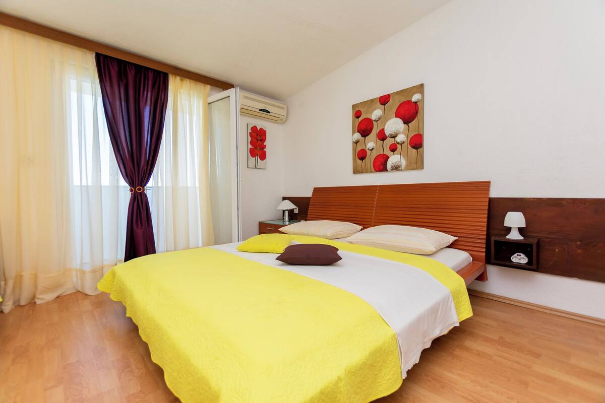 A neatly made bed with a yellow bedspread, a wooden headboard, and a nightstand with a lamp.