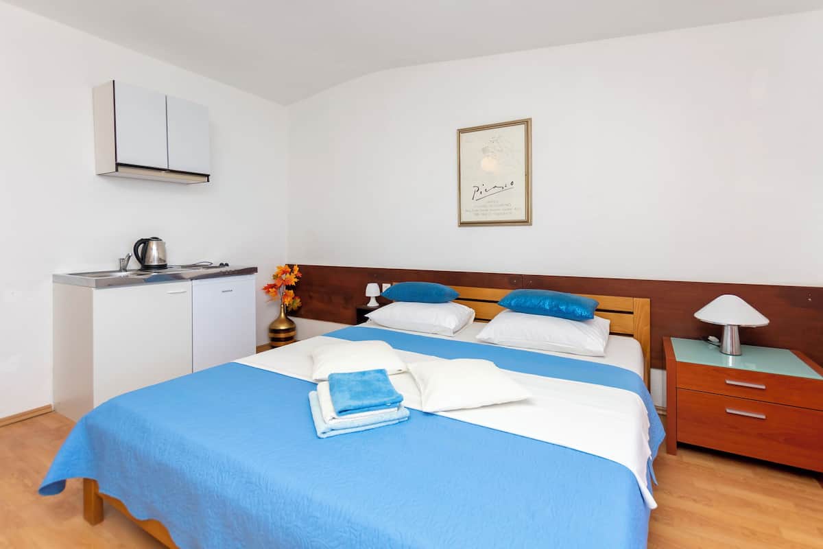 A neatly arranged bedroom with a bed, bedside table, and a small kitchenette.