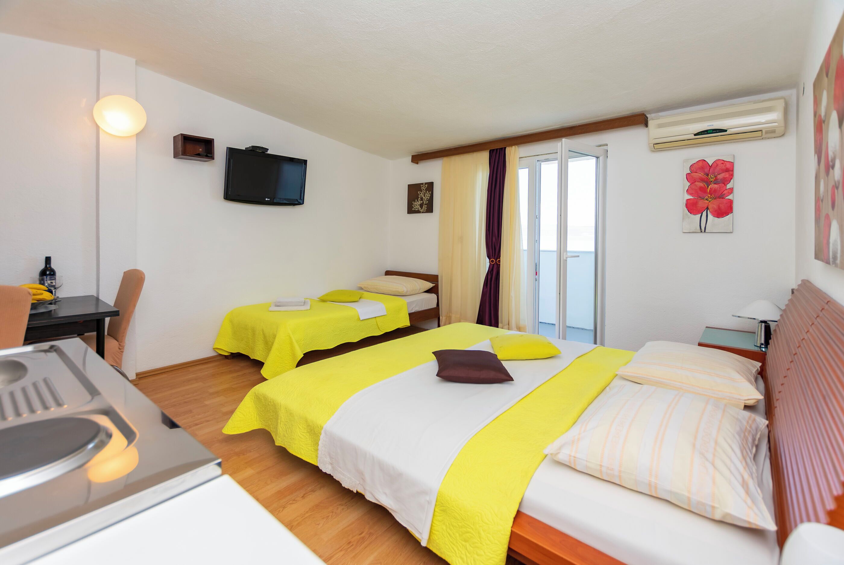 A hotel room with two beds, a TV, a desk with a sink, and a window with curtains.