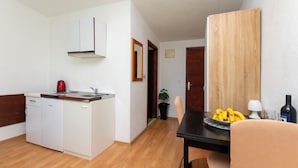 A compact kitchen with white appliances, a dining area with a table and chairs, and a wooden panel on the wall. - Apartments Luka (Dugi Rat)