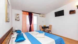 A hotel room with a bed, a desk, a chair, a TV, and a window with curtains. - Apartments Luka (Dugi Rat)