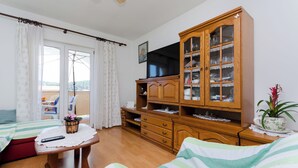 Ein Zimmer mit einem Bett, einem Holzschrank, einem Fernseher und einem Balkon mit Vorhängen.