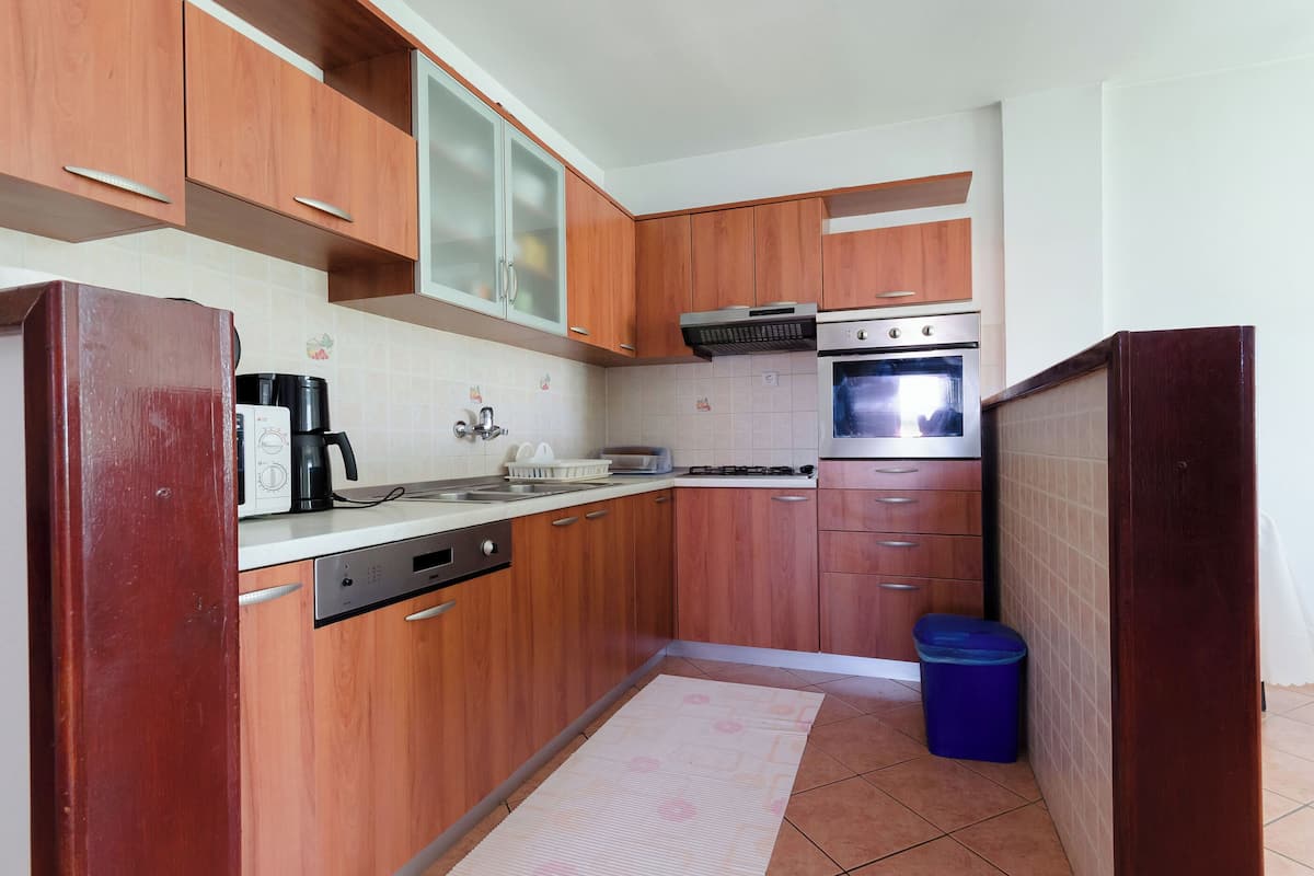 A compact kitchen with wooden cabinets, a dishwasher, a stove, and a trash bin.