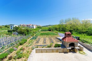 A residential area with a stone-built outdoor oven, a vegetable garden, and a backdrop of houses. - Apartments and Room Sime M (Lopar)