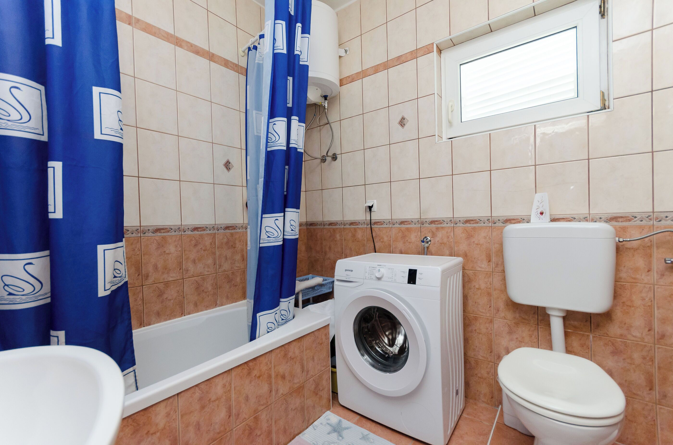 A bathroom with a washing machine, toilet, bathtub, and blue shower curtains.