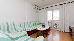 Ein Wohnzimmer mit gestreiften, grün-weißen Sofas, einem Holztisch und einer Glastür, die zu einem Außenbereich führt.