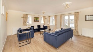 A spacious living room with a blue sofa, a coffee table, and a TV. There are curtains on the windows, and a painting on the wall. - Riverside Home in Perth (Perth)