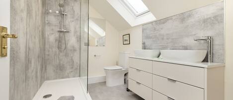 Un baño moderno con tragaluz, ducha con cerramiento de vidrio, lavamanos blanco y un espejo grande.