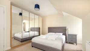 A bedroom with a large mirror, a bed with white linens, a nightstand, and a lamp. - Riverside Home in Perth (Perth)