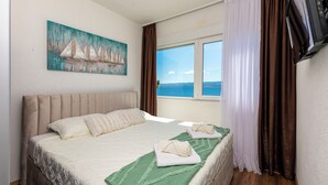 A bedroom with a bed, a painting of sailboats, a TV, and a window with curtains. - Apartment Filip (Dugi Rat)