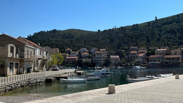A waterfront promenade with hexagonal paving, a stone building with a staircase, and a backdrop of hillside buildings. - Apartment Nela (Smokvica)