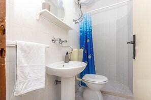 A bathroom with a white sink, toilet, and blue shower curtain. - Apartment Nela (Smokvica)