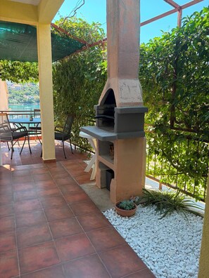 An outdoor patio with a stone-tiled floor, a grill, and a table with chairs. - Apartment Nela (Smokvica)