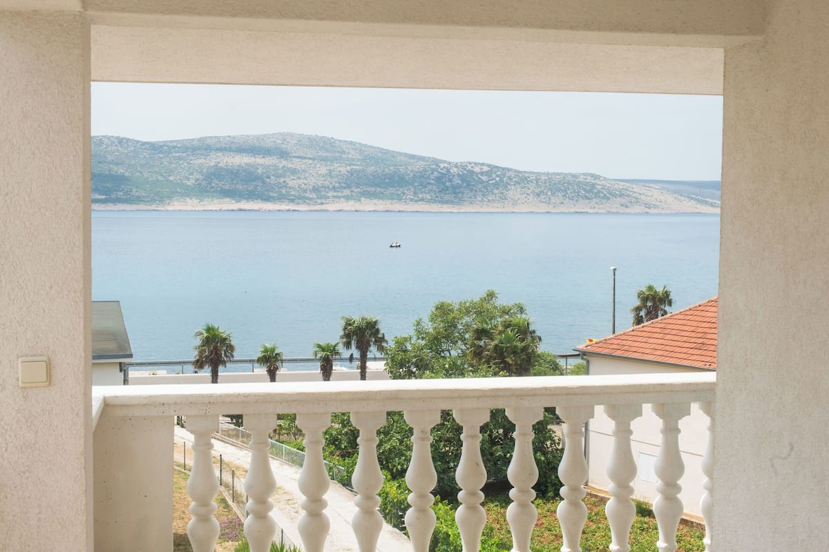 A balcony with a view of a calm sea and distant hills.