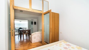 Ein Schlafzimmer mit einem Bett, einem kleinen Tisch und einem Stuhl. Eine Schiebetür führt zu einem Balkon mit Tisch und Stühlen.
