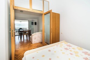 A bedroom with a bed, a small table, and a chair. There is a sliding door leading to a balcony with a table and chairs. - Apartments More Sunce (Starigrad)