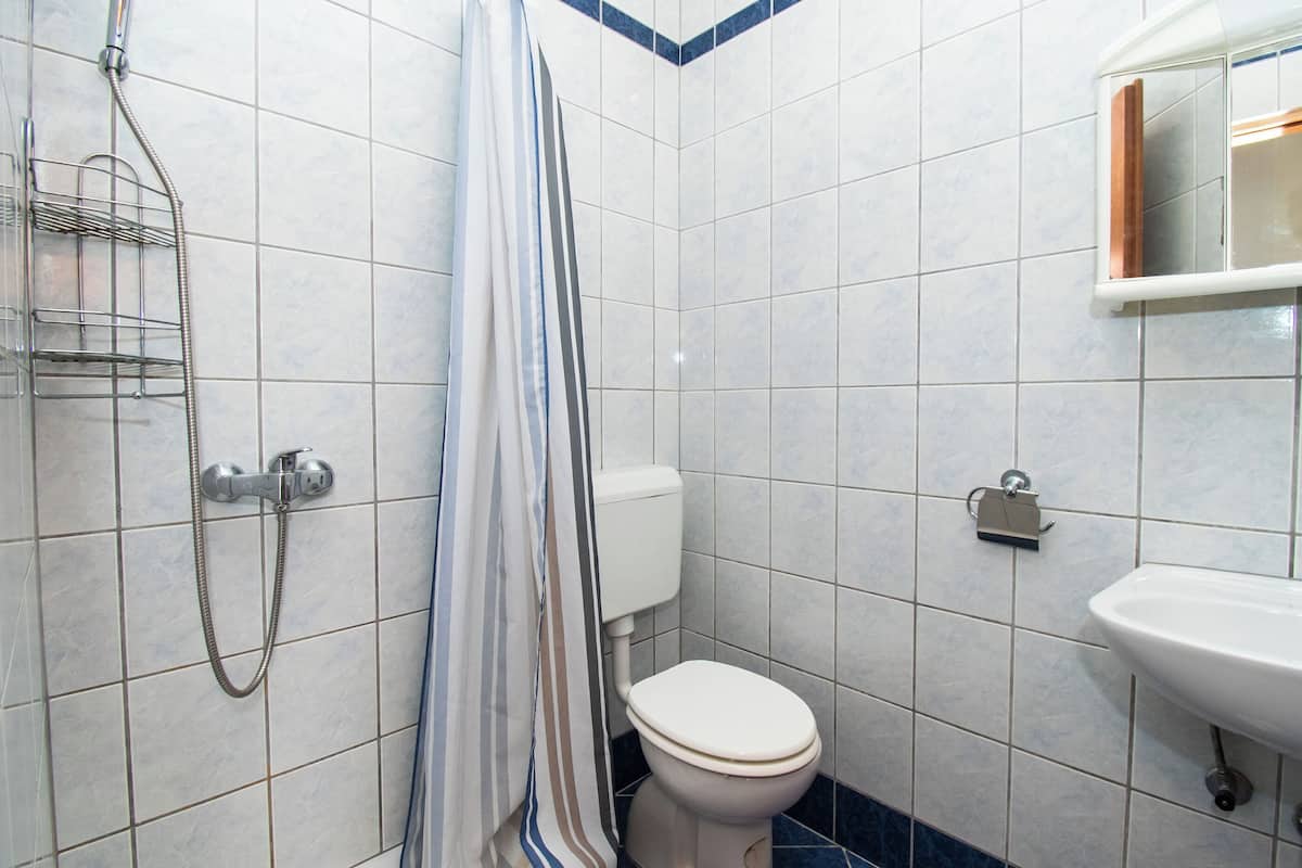 A bathroom with white tiled walls, a shower with a metal rack, a toilet, and a sink with a mirror above it.