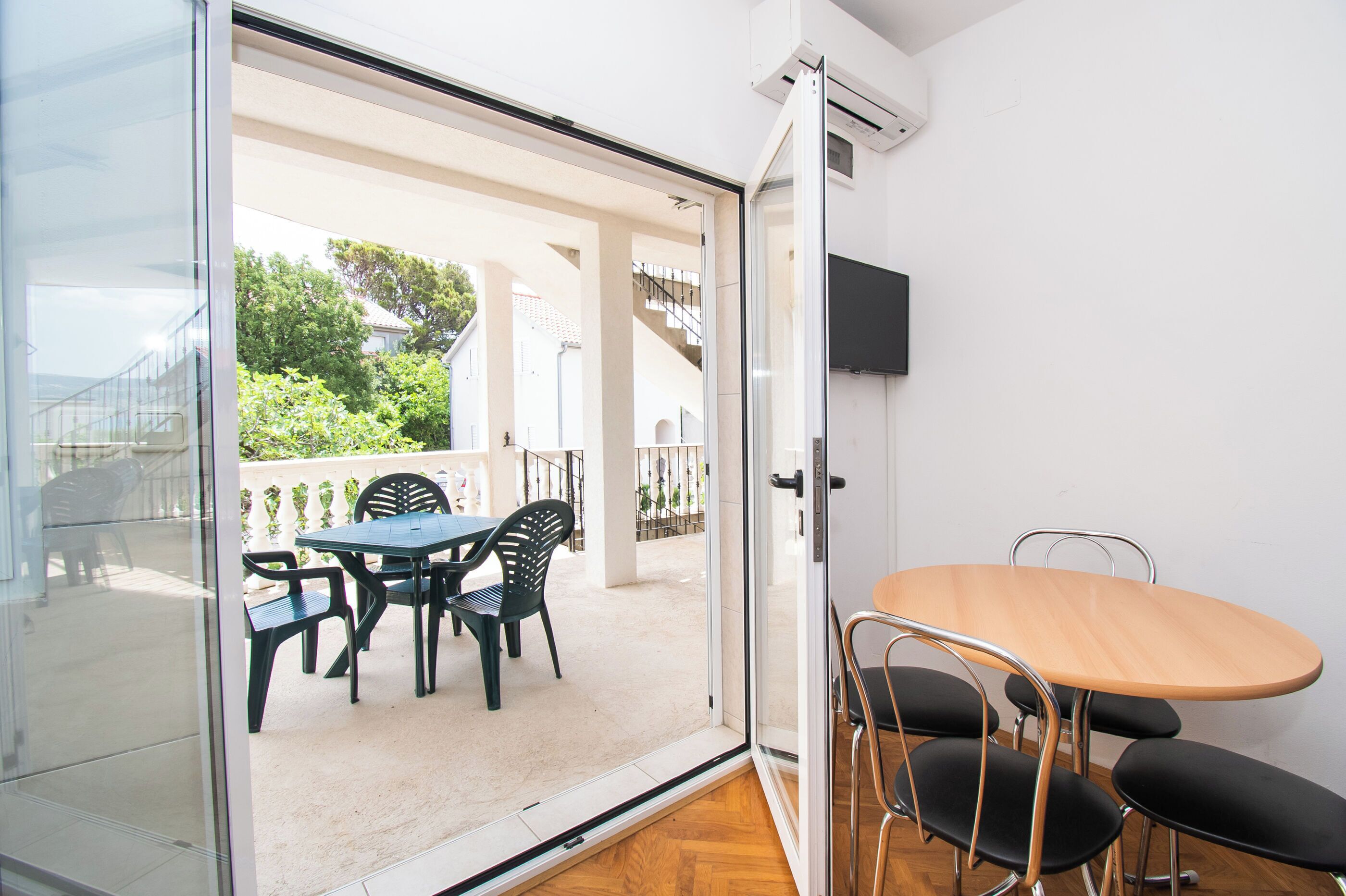 Een kamer met een schuifdeur die leidt naar een terras buiten, met een tafel en stoelen.