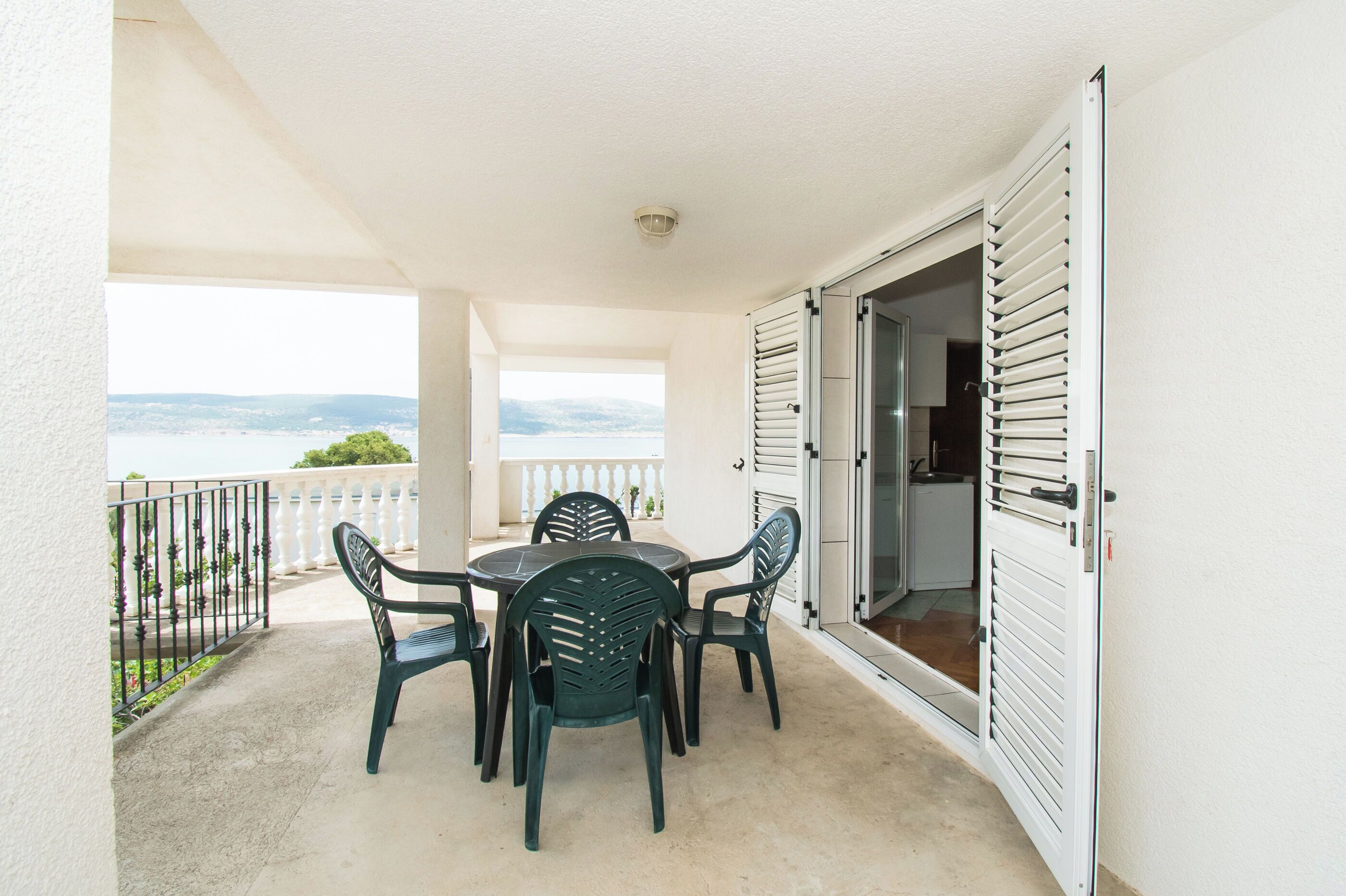 A balcony with a table and chairs, a white door, and a view of the sea.