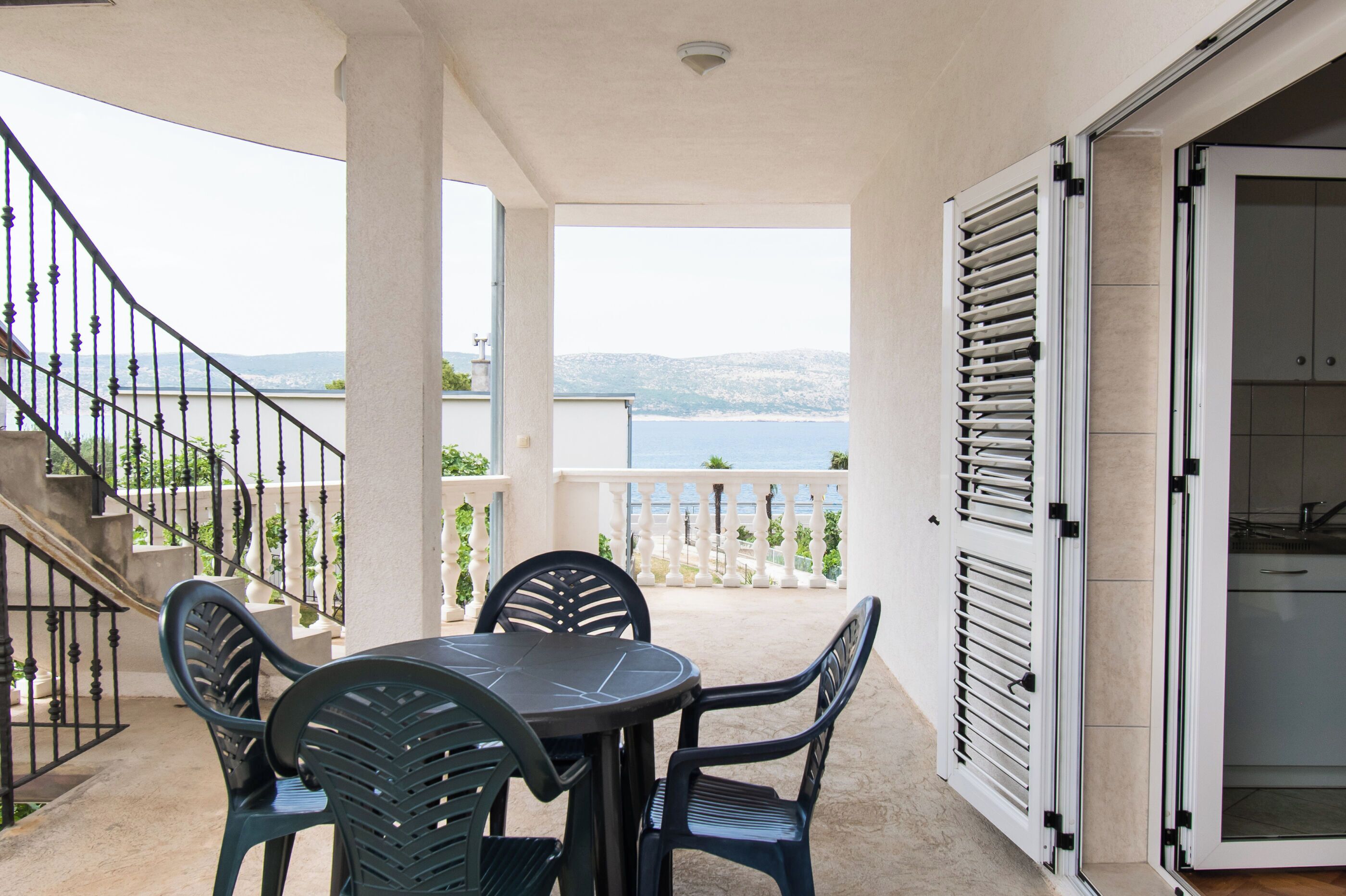 A balcony with a table and chairs, a view of the sea, and a staircase leading to an upper level.