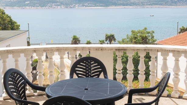 Ein Balkon mit Tisch und Stühlen mit Blick auf ein Gewässer und hügelige Landschaft.