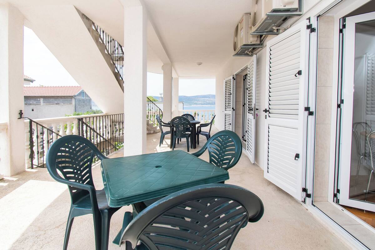 A balcony with a table and chairs, a staircase, and a view of the sea.