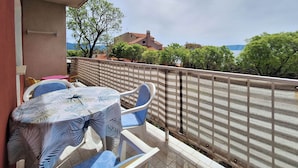 A balcony with a table and chairs, a view of trees and buildings, and a clear sky. - Apartment Sandra (Novi Vinodolski)