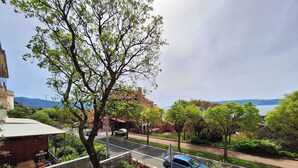 A street view with a tree-lined sidewalk, a parked car, and a building with a sign advertising free apartments. - Apartment Sandra (Novi Vinodolski)