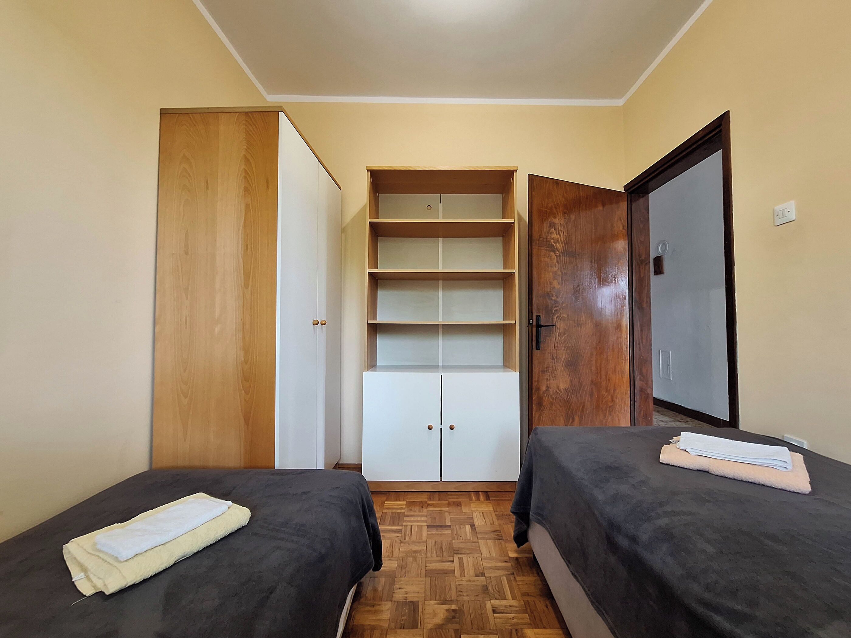 A bedroom with two beds, a wardrobe, and a built-in shelving unit.