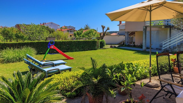 A well-maintained garden with a play area, including a slide and swings, and a covered seating area with an umbrella. - Apartments Tanya (Rab)