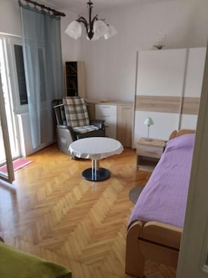 Ein Schlafzimmer mit Bett, Stuhl, kleinem Tisch, Kleiderschrank und Deckenleuchte.