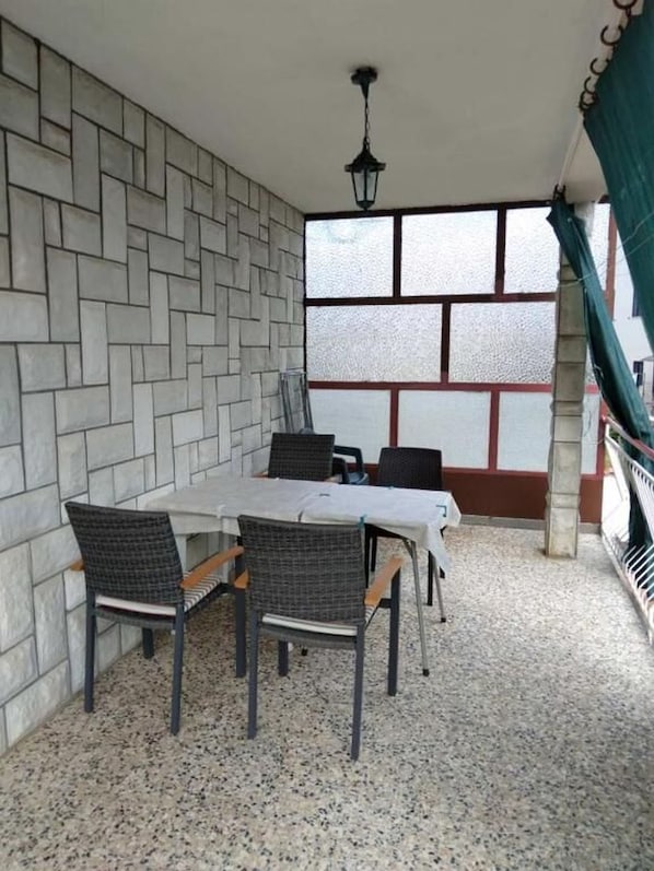 An outdoor patio with a table and chairs, a stone wall, and a view through a window with frosted glass panels. - Apartments Sea Breeze (Umag)