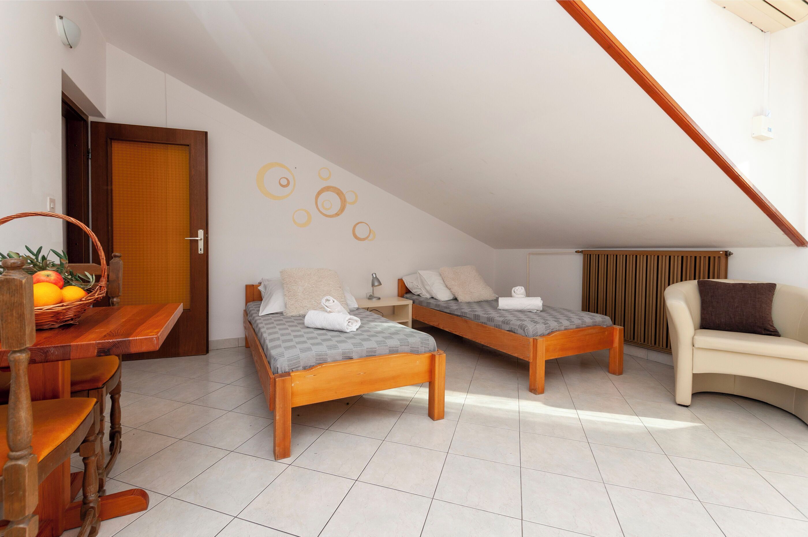 A room with two wooden beds, a wooden dining table with fruit, a chair, and a sofa.