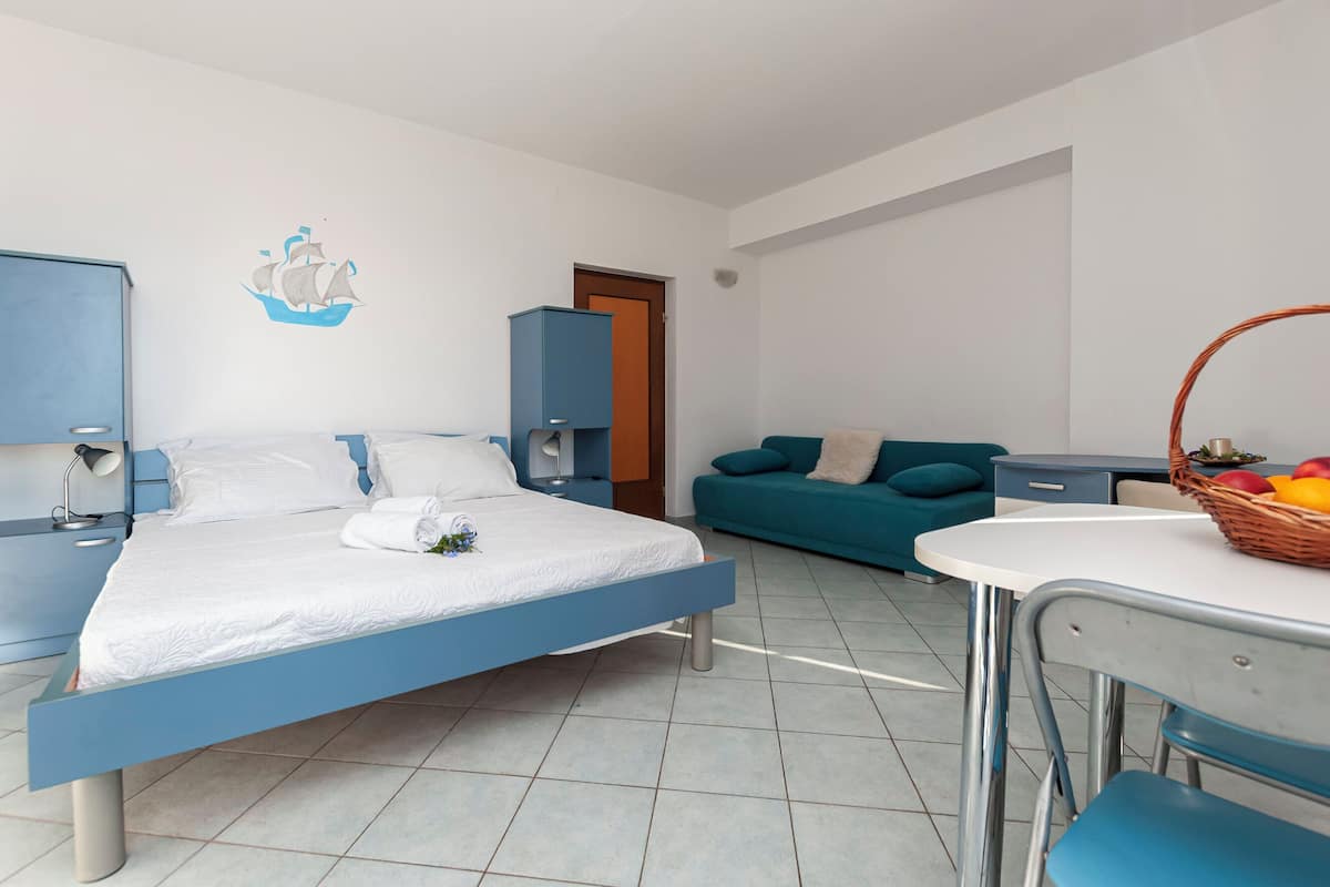 A modern bedroom with a bed, a blue sofa, a small table with a fruit basket, and a wall decoration of a sailboat.