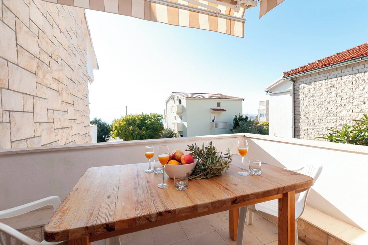 A wooden table with a bowl of fruit and glasses of orange juice on an outdoor balcony.