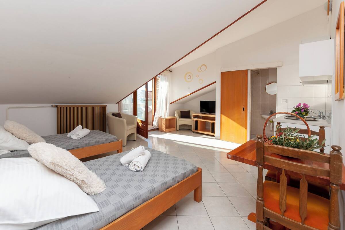A modern hotel room with two beds, a desk, a chair, and a kitchenette.